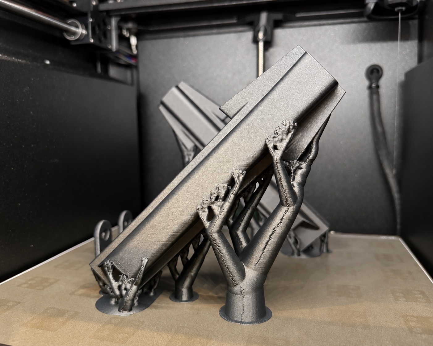 A carbon-fiber drone arm on tree supports inside a 3D printer